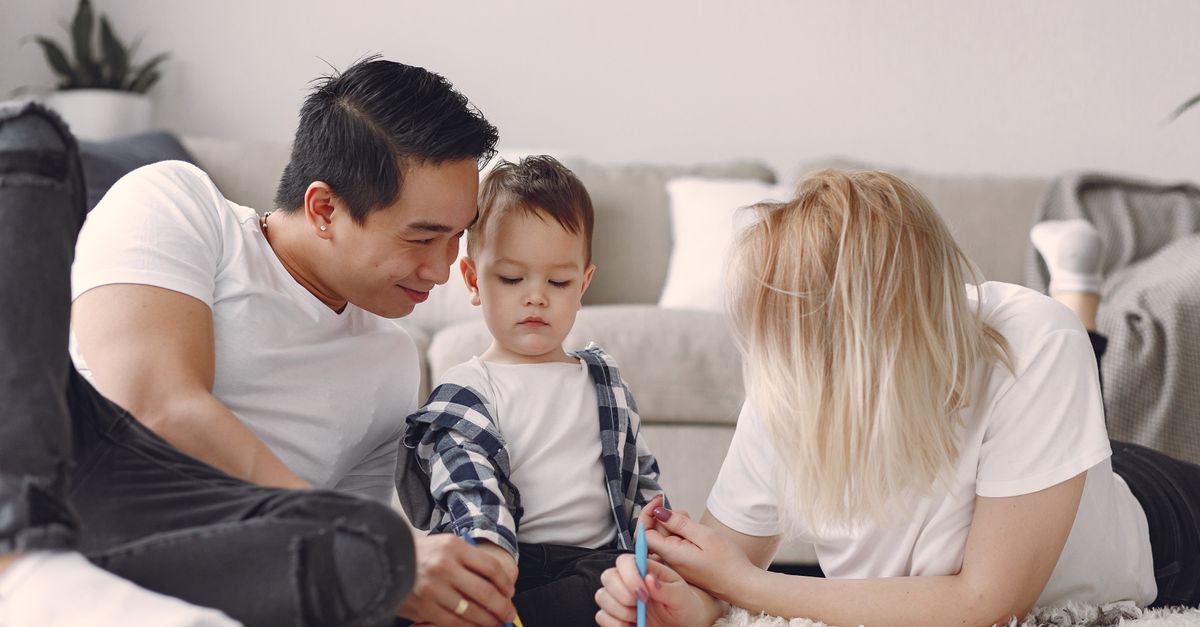 Two parents and their young child drawing together on the floor at home.