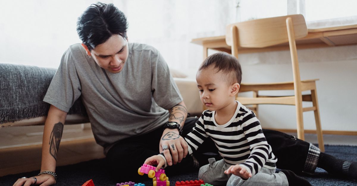 A caregiver and a young child working on a hands-on learning activity together on the floor at home.